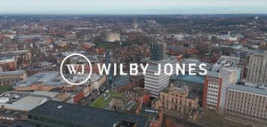 Aerial view of Norwich city centre with Wilby Jones logo overlay, showing historic castle, cathedral spire, and mixed residential and commercial buildings.